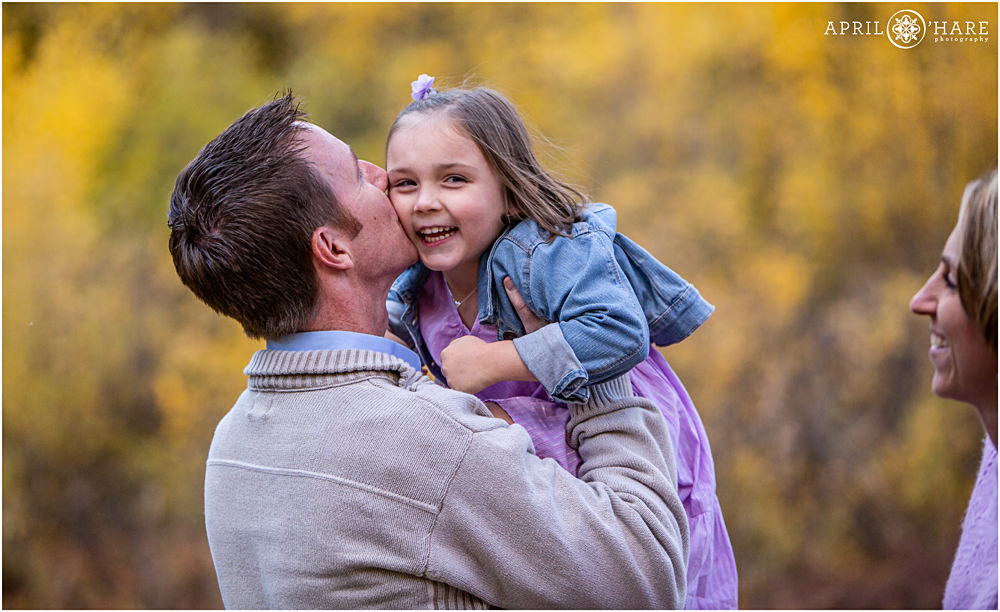 A girl smiles as her dad gives her a kiss on the cheek during fall color family photos on Guanella Pass
