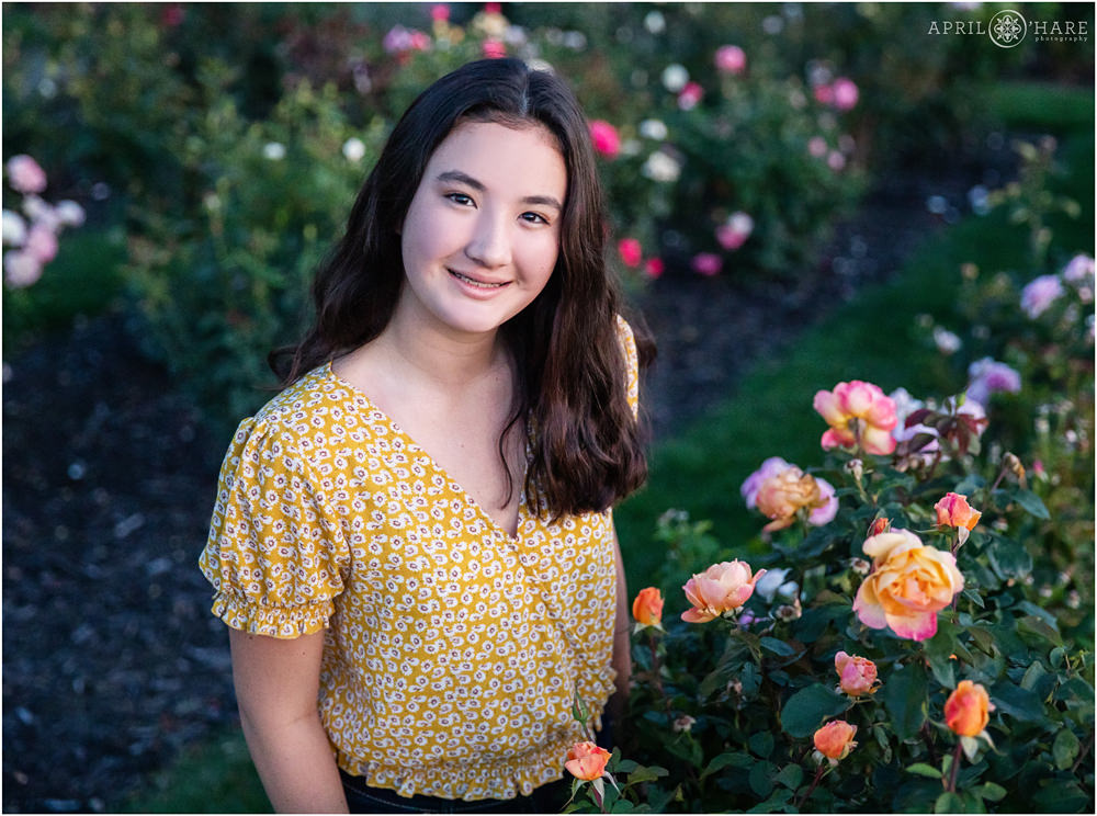 Pretty teenage girl with yellow top poses in a rose garden at City Park in Denver Colorado at her family portrait session