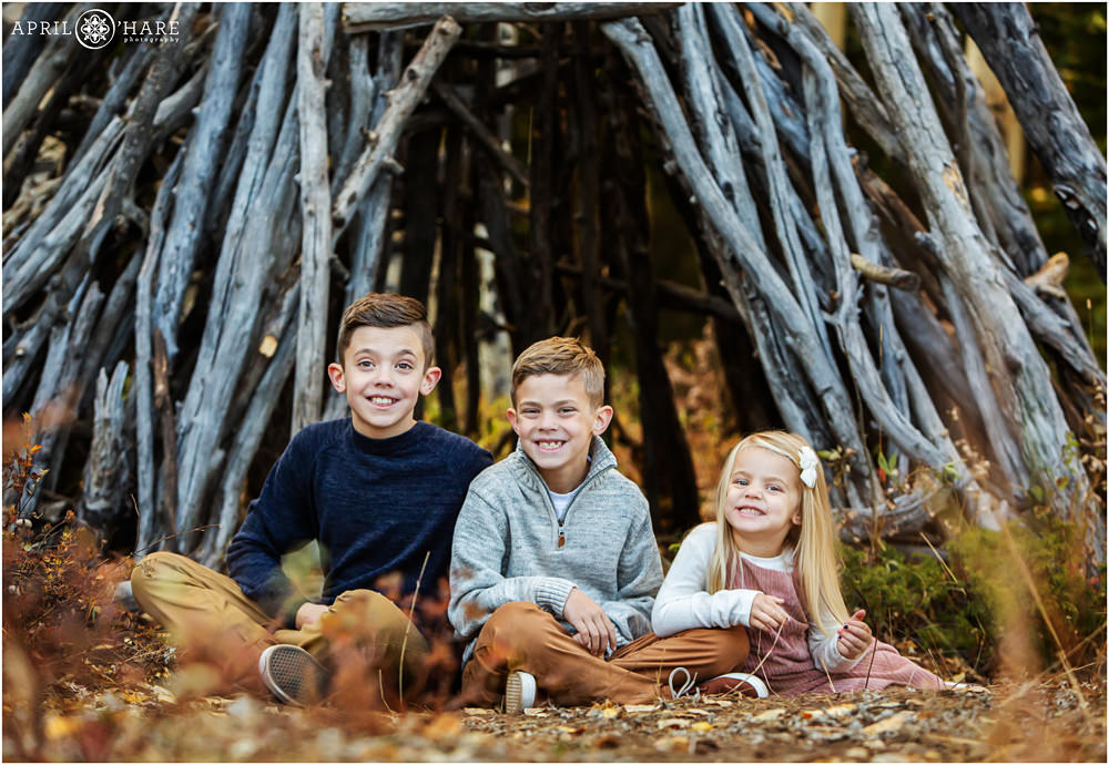 Cute photo of kids sitting in front of a wood tipi at the Beaver Brook Watershed Trail in Evergreen CO
