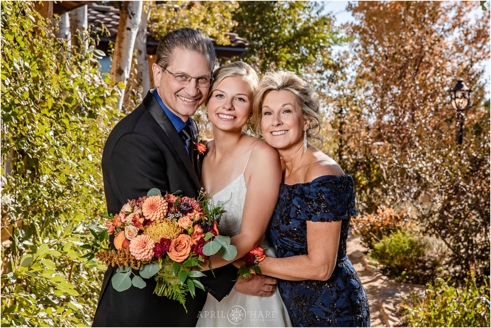Bride with pretty orange bridal bouquet by Project Floral poses for family photo with her parents at Villa Parker