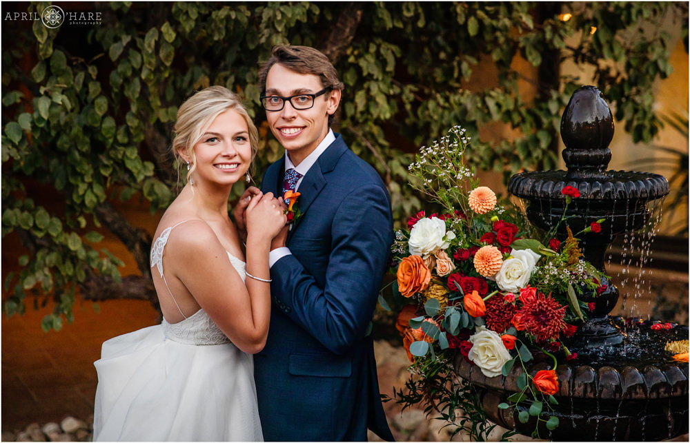 Adorable couple clasp hands next to their pretty orange florals on a fountain in the courtyard at Villa Parker