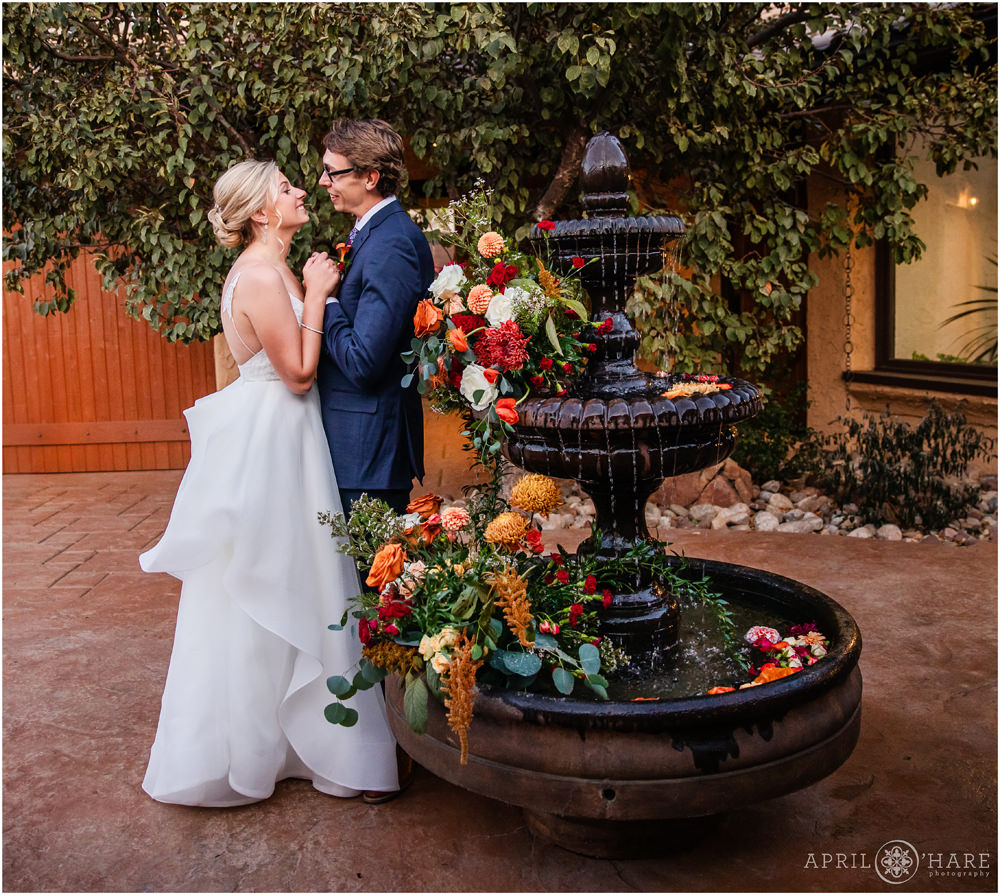 Romantic wedding portrait of bride and groom holding hands next to their pretty orange floral fountain in the courtyard at Villa Parker in Colorado