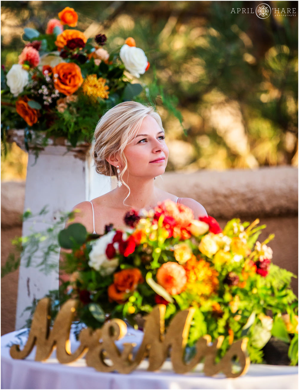 Beautiful blonde bride sits at the head table decorated with orange florals at her fall wedding at Villa Parker in Colorado