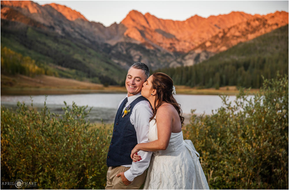 Sweet portrait of bride kissing her groom with a pretty orange alpenglow mountain backdrop in Vail
