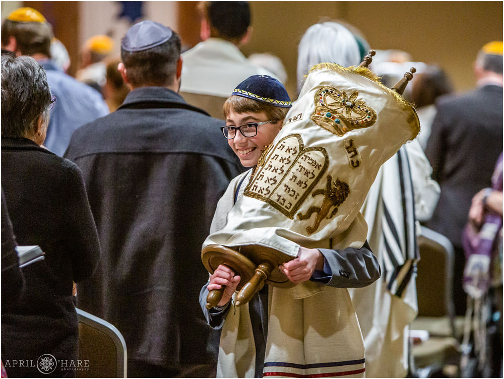A young bar mitzvah man carries the Torah on his shoulder throughout the room at his bar mitzvah in Fort Collins Colorado