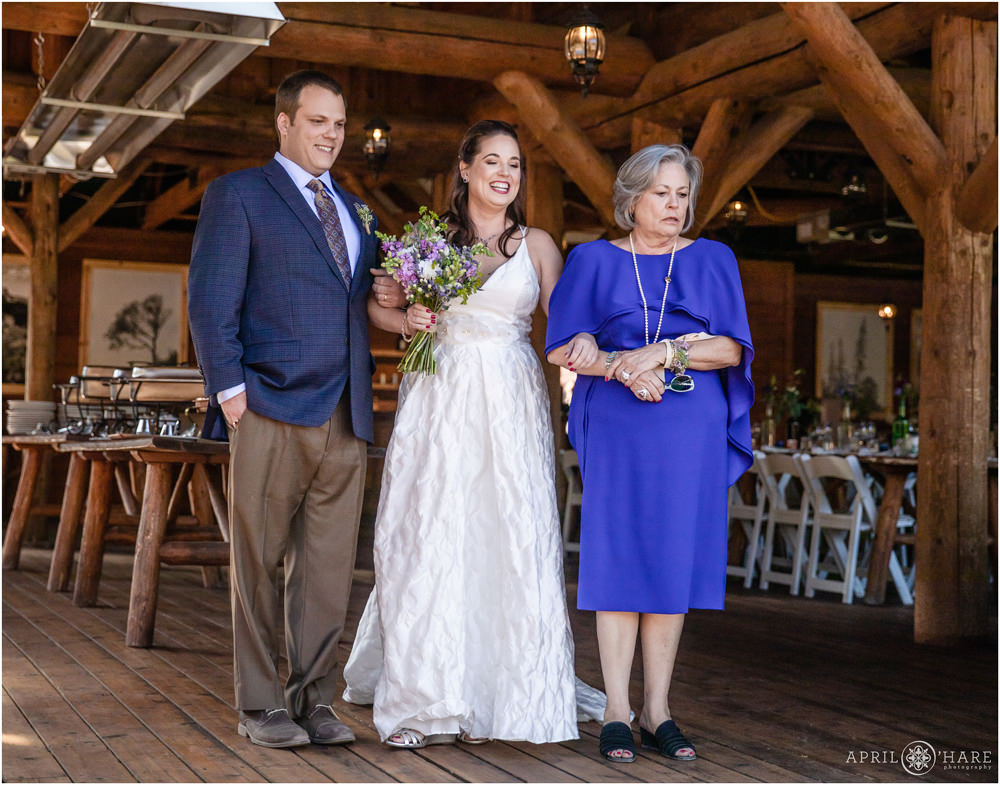Bride laughs at her flower girl niece before walking down the aisle with her mom and brother at Piney River Ranch