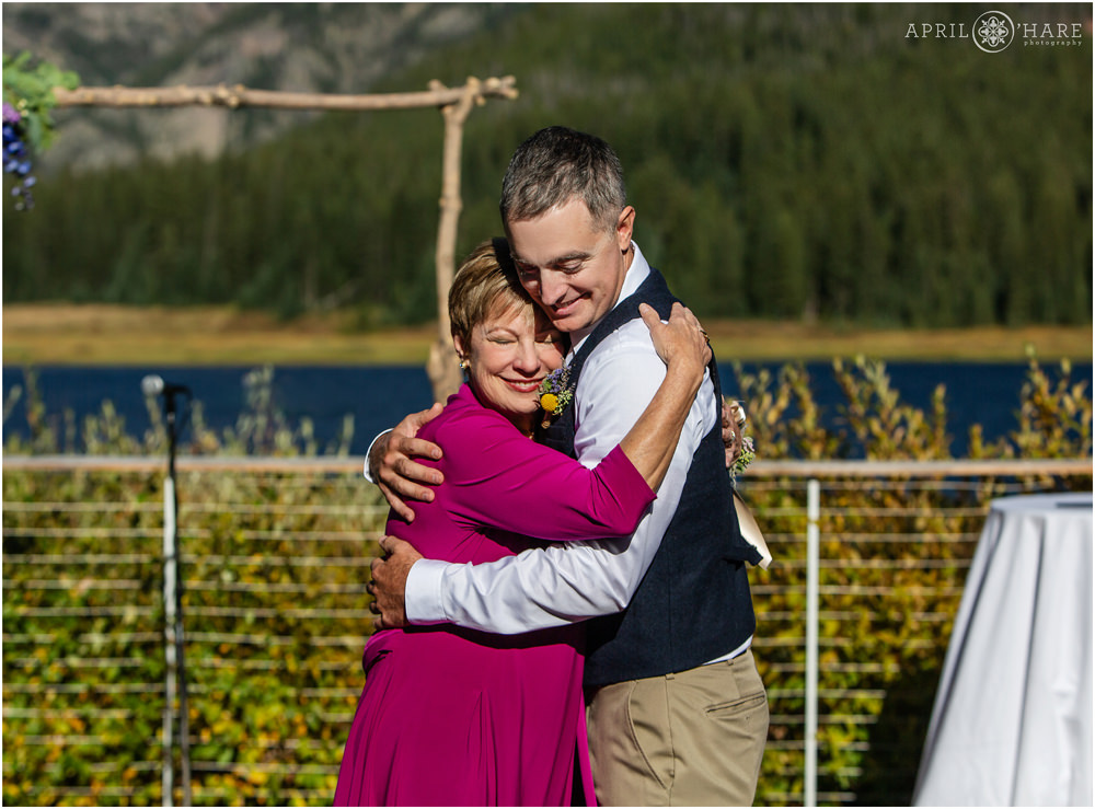 Groom and his mom hug on a bright sunny outdoor wedding ceremony moment in Colorado