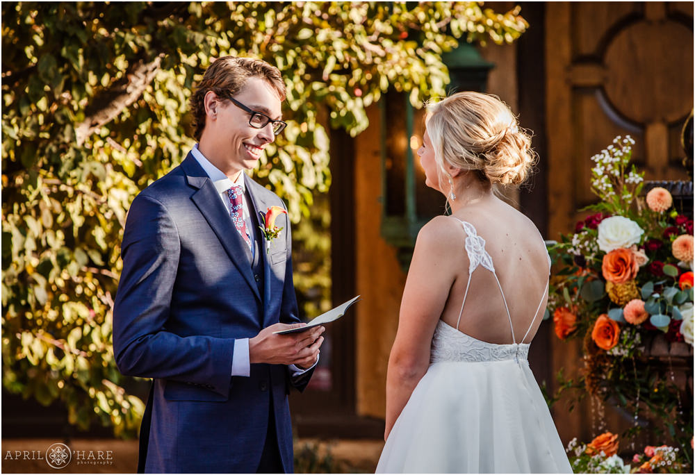 Groom smiles at bride as he says his vows in the courtyard at Villa Parker in Colorado