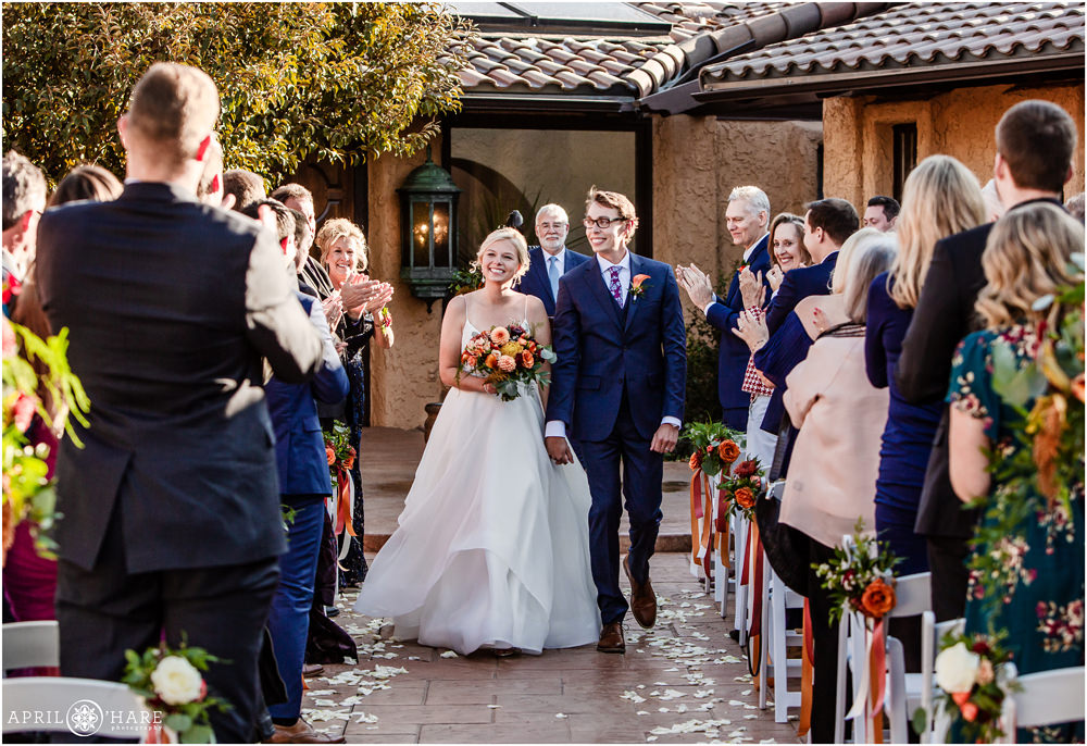 Happy bride and groom walk hand in hand down the aisle at their pretty fall wedding in the courtyard at Villa Parker in Colorado