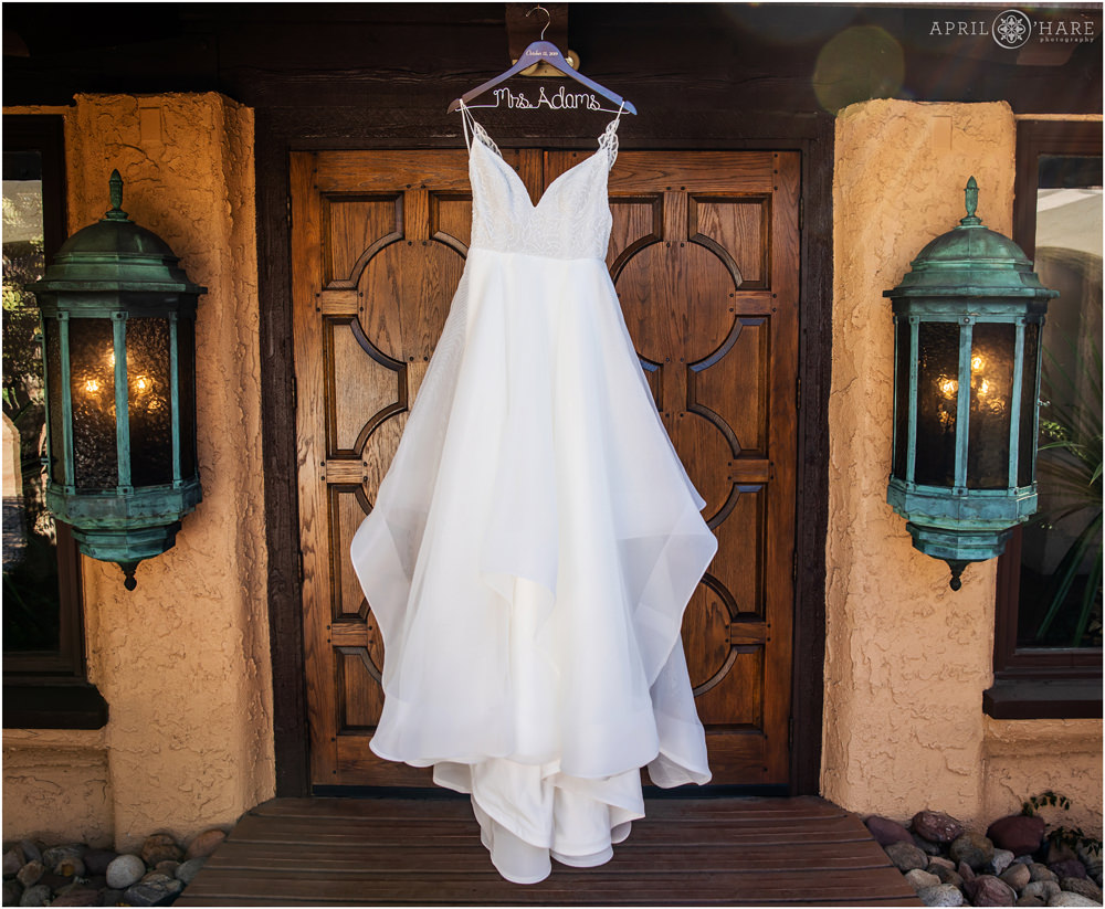 Gorgeous Hayley Paige wedding gown from Anna Be hangs in front of carved wood doors at Villa Parker wedding venue in Colorado