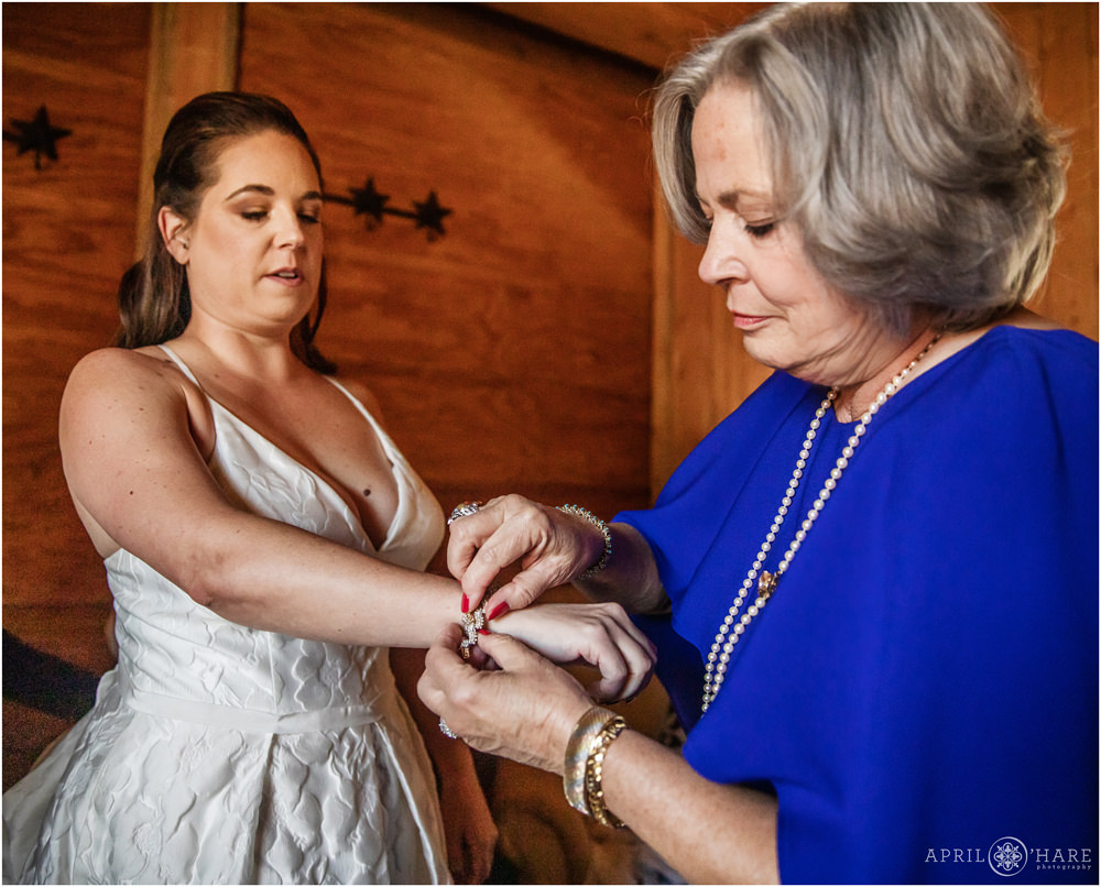 Mom helps her daughter with a pretty bracelet at her rustic fall wedding in Vail