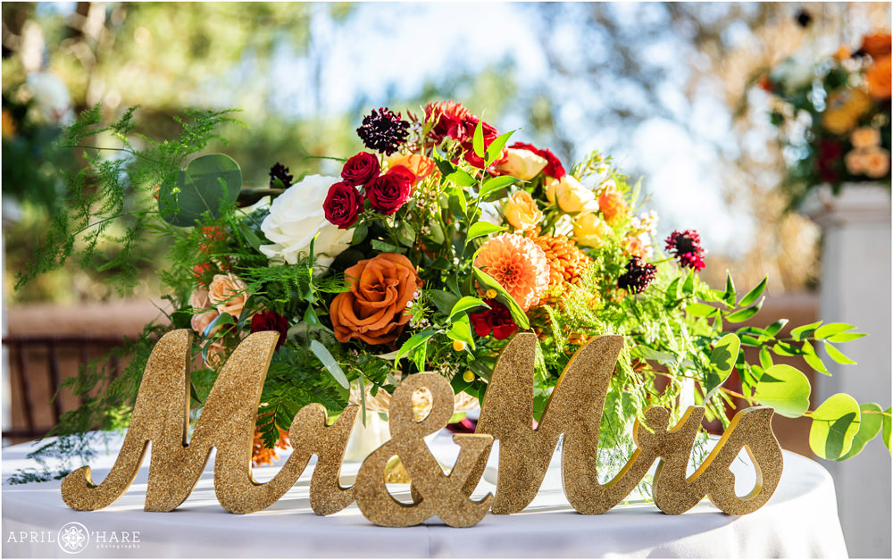 Gold Glitter Mr and Mrs Cursive Letters and orange florals decorate a Sweetheart table at a Villa Parker Wedding Reception in Colorado