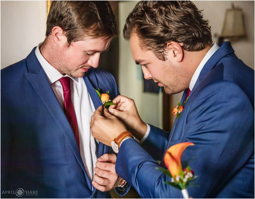 Groomsmen help each other with orange boutonnieres at Villa Parker in Colorado