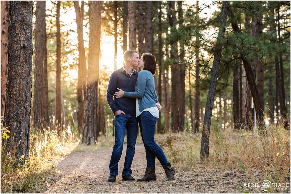 Couple portrait kissing in a pine forest with pretty light streaming through trees in Colorado Springs