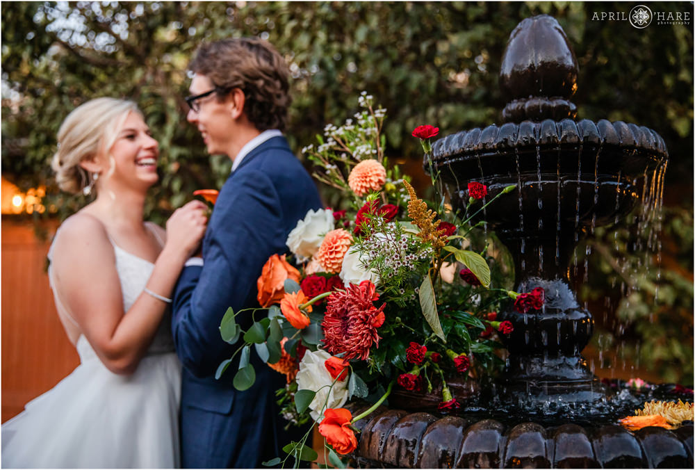 Close up of orange florals on fountain with bride and groom laughing in the backdrop at Villa Parker