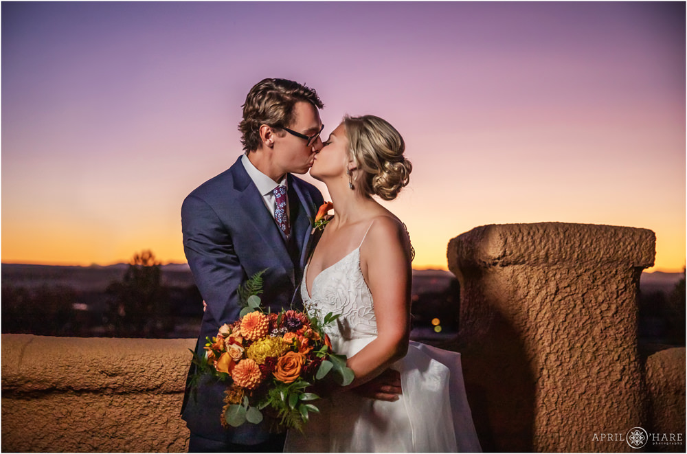 Beautiful purple and orange sunset matches the orange and purple fall color bouquet of bride and groom as they kiss at Villa Parker