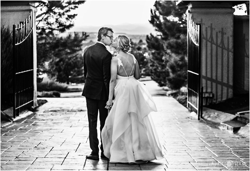 Romantic B&W photo of bride and groom kissing at sunset in front of the gates at Villa Parker in Colorado
