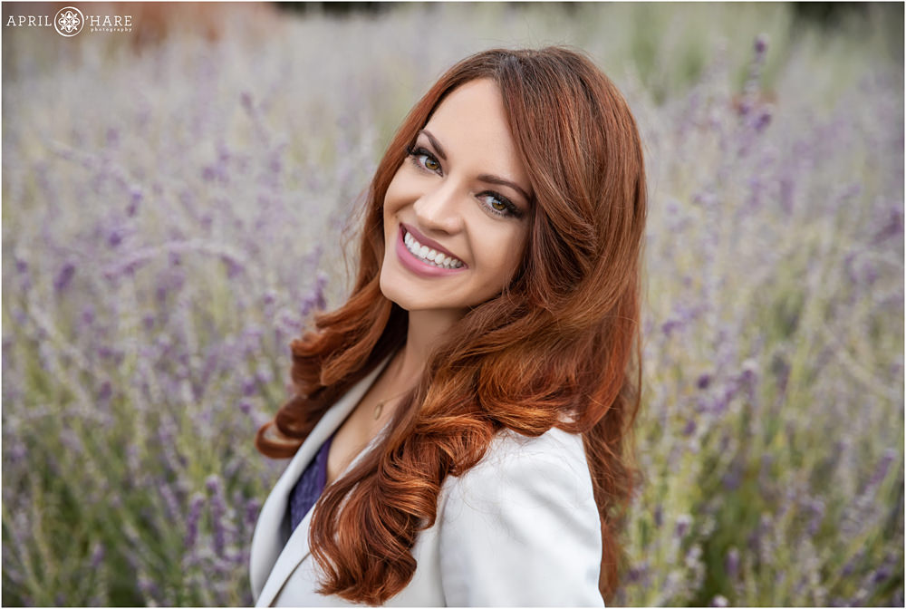 A woman with red hair poses for a headshot photo in front of russian sage plant at Centennial Gardens in Colorado