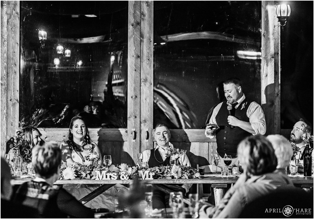 B&W wedding photo of a best man giving a speech during a rustic wedding reception in Vail