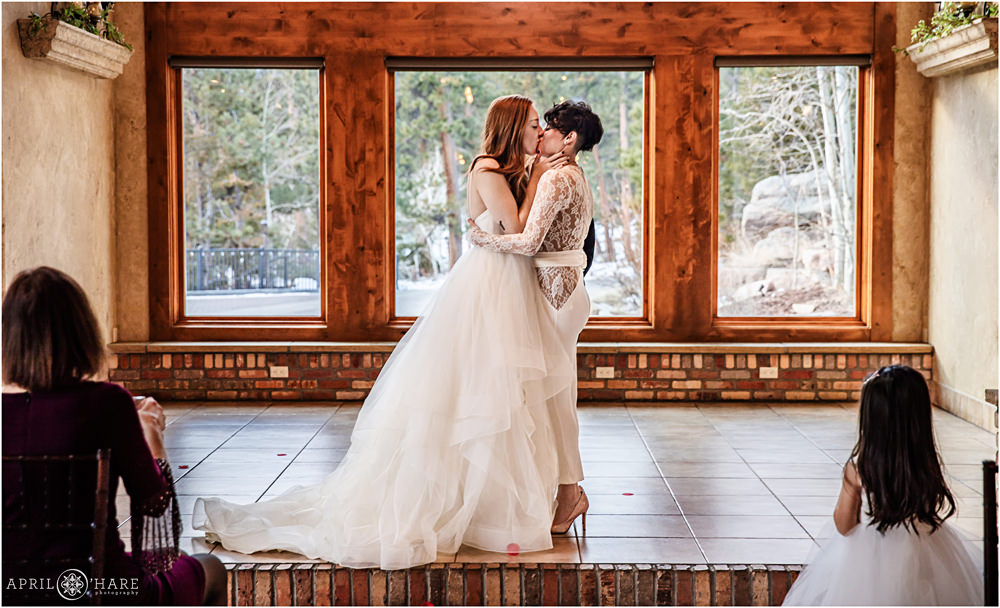 Two brides kiss at their beautiful indoor mountain wedding at Della Terra