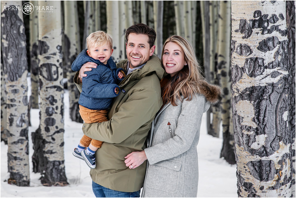 Adorable family photo with happy toddler boy in a snowy aspen tree grove in Colorado