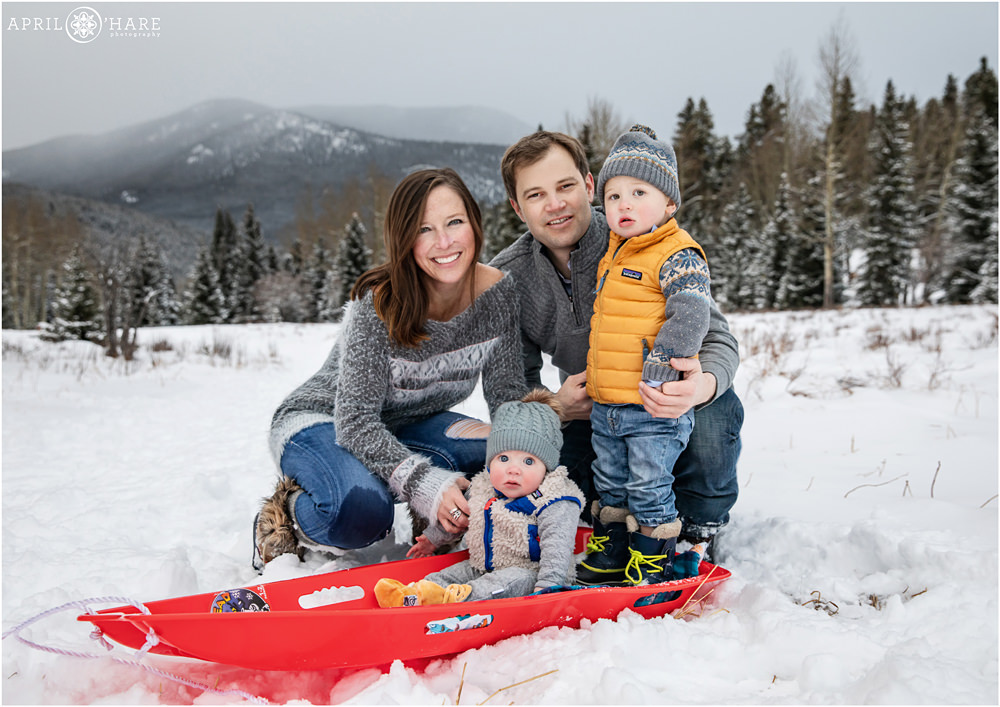 Adorable family photo with two sons on a red sled in the mountains of Colorado during winter