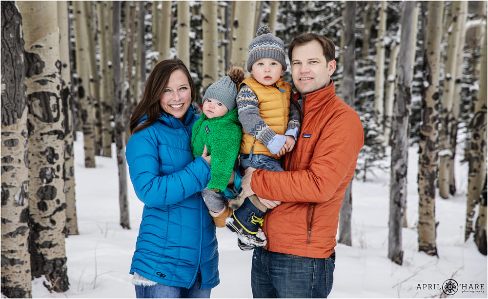 A family wearing colorful winter gear pose for portraits in an aspen tree forest in Colorado