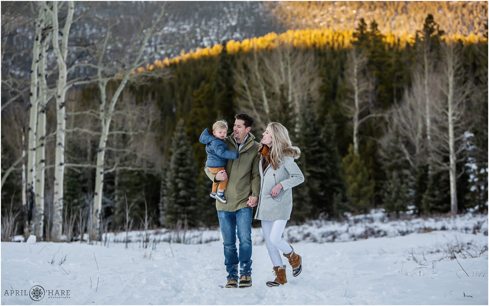 Cute family walk on a snow covered trail with their toddler son during winter in Colorado