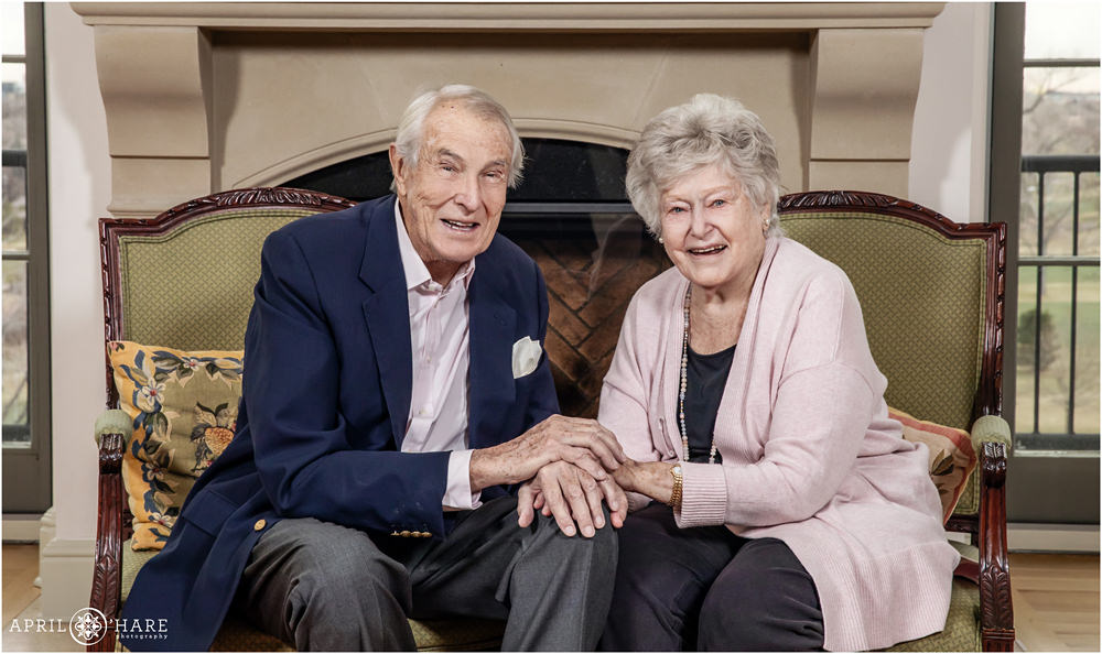 A cute portrait of grandparents laughing together as they pose in front of their fireplace in Denver Colorado