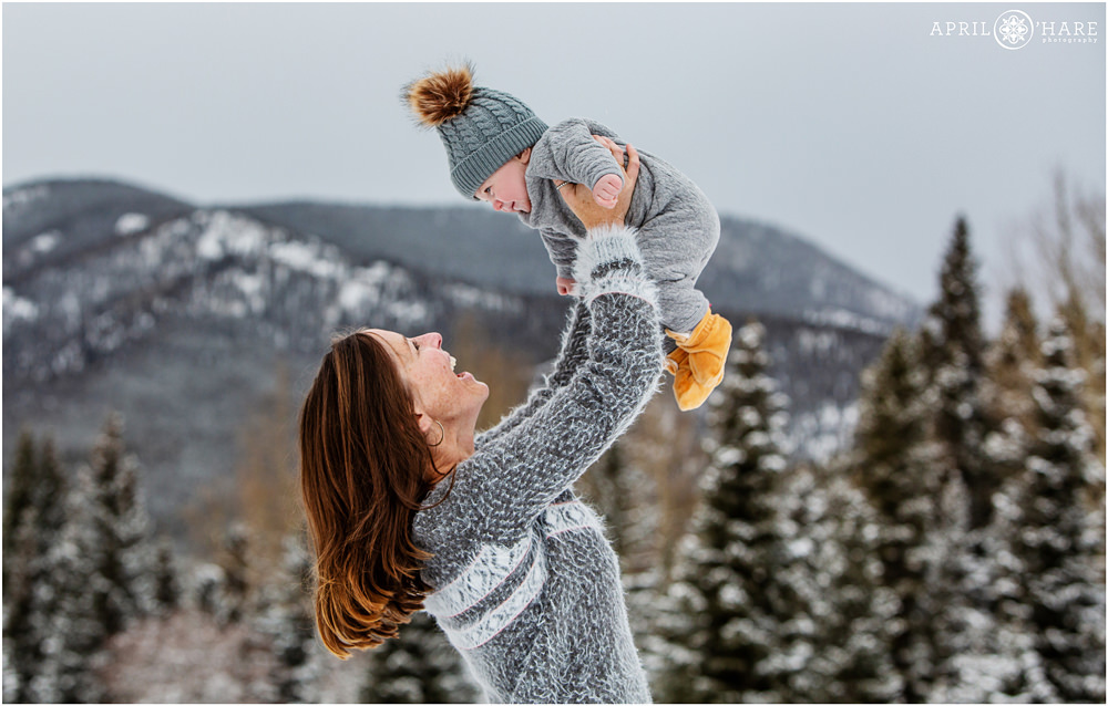 Mom holds her baby up in the air during a winter family portrait session in Colorado mountains