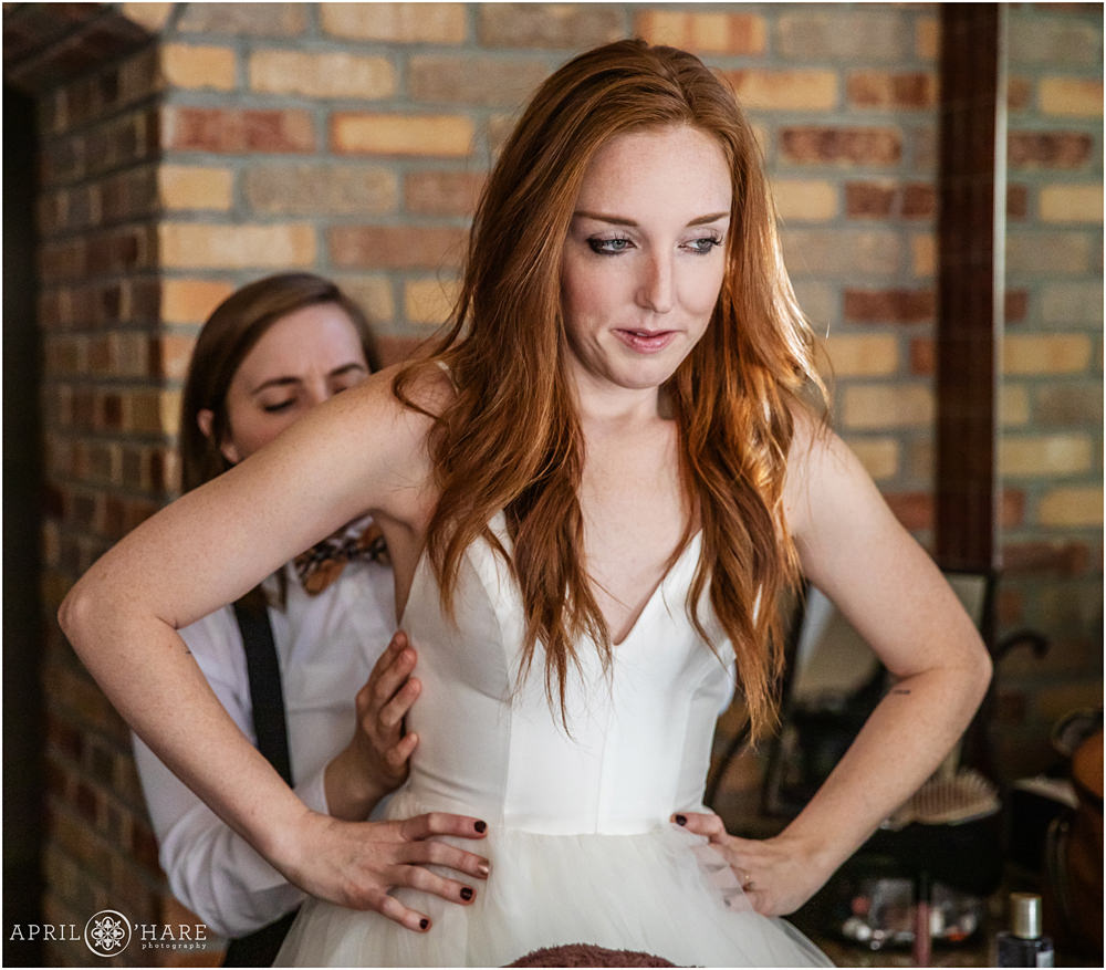 Beautiful red head bride gets help with her dress from her sister at Della Terra