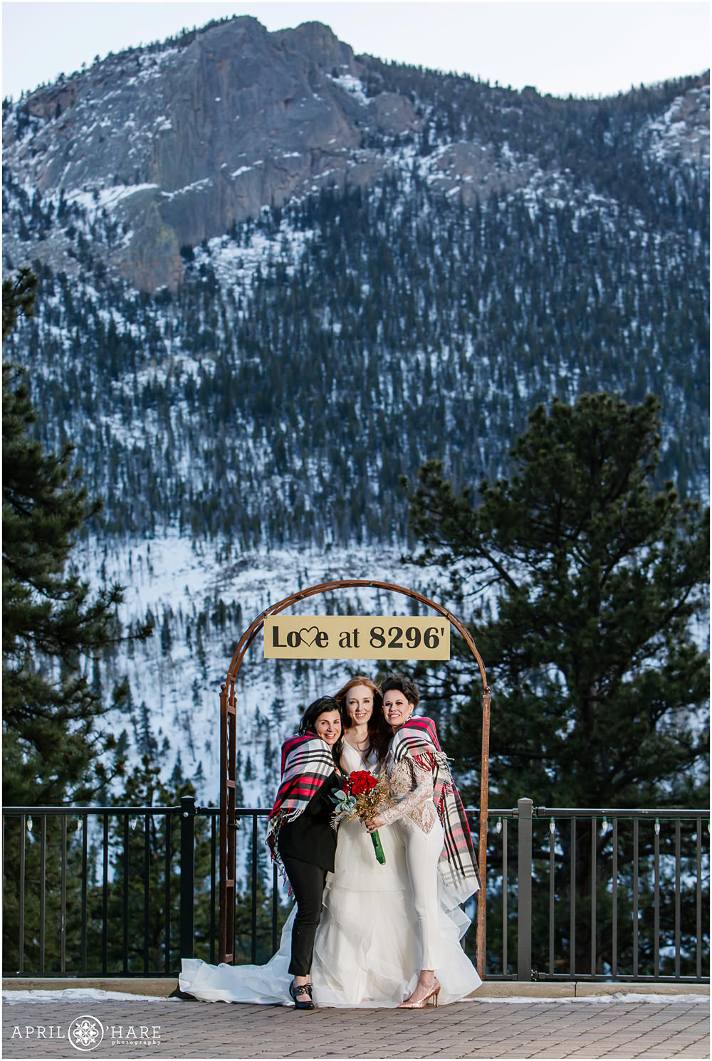 Two brides and their officiant aunt pose under the Love at 8296 arch at Della Terra Mountain Chateau