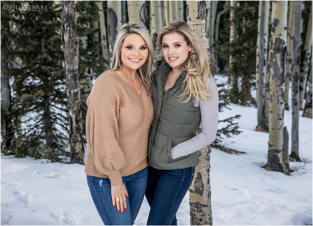 Two adult sisters pose for family photo in a forest in Colorado with aspen trees