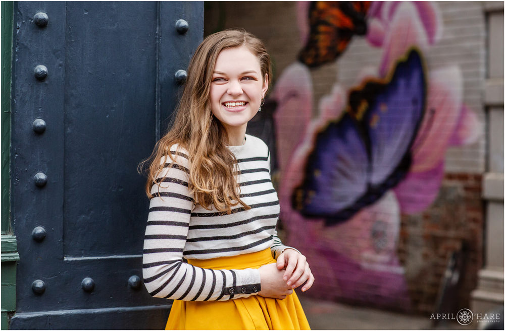 Cute candid senior photo of a girl in downtown Denver with a pretty floral butterfly mural backdrop