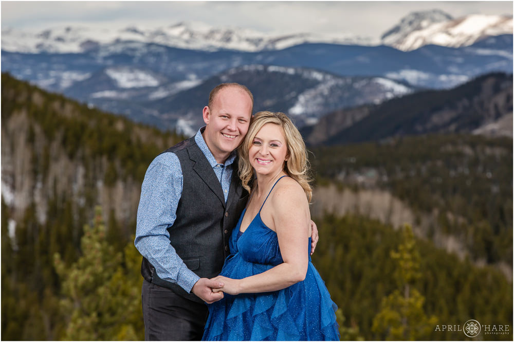 Cute couple wearing blue pose for portraits in front of a pretty blue mountain backdrop in Colorado