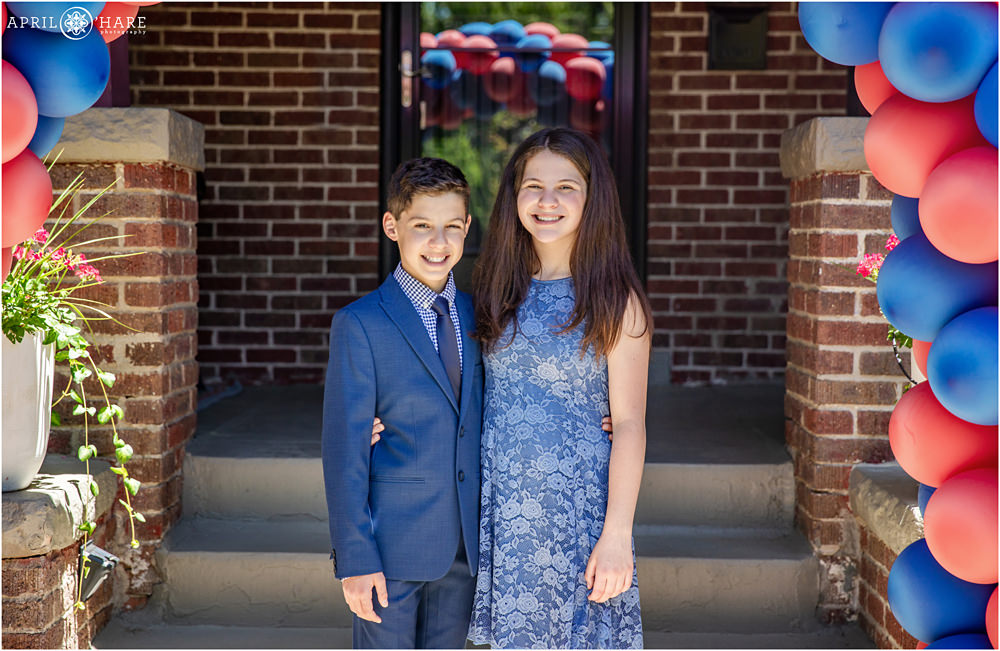 Twins pose for a portrait on the day of their Denver B'nai Mitzvah in Colorado on their front porch decorated with red & blue balloons