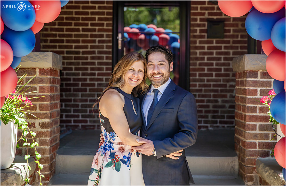 Parents pose for a portrait in front of their house decorated with red and blue balloons for their twins' b'nai mitzvah