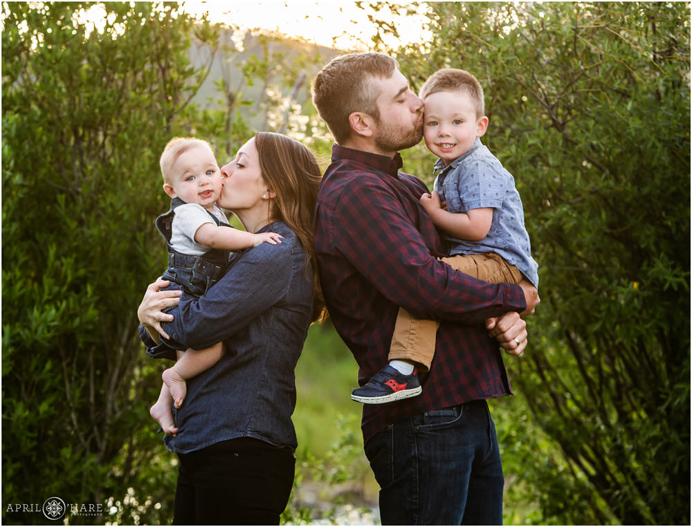 Mom and Dad give their two young sons a kiss at their Granby Colorado family photography session during summer