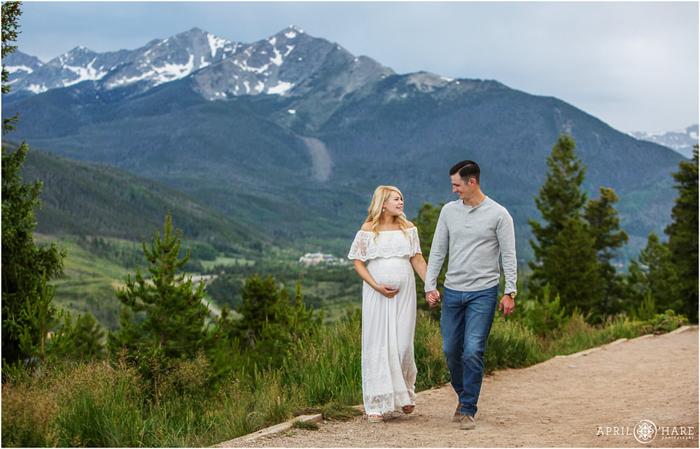 Pregnant mother to be holds hands with her husband as they walk down the path at Sapphire Point with a pretty blue mountain backdrop