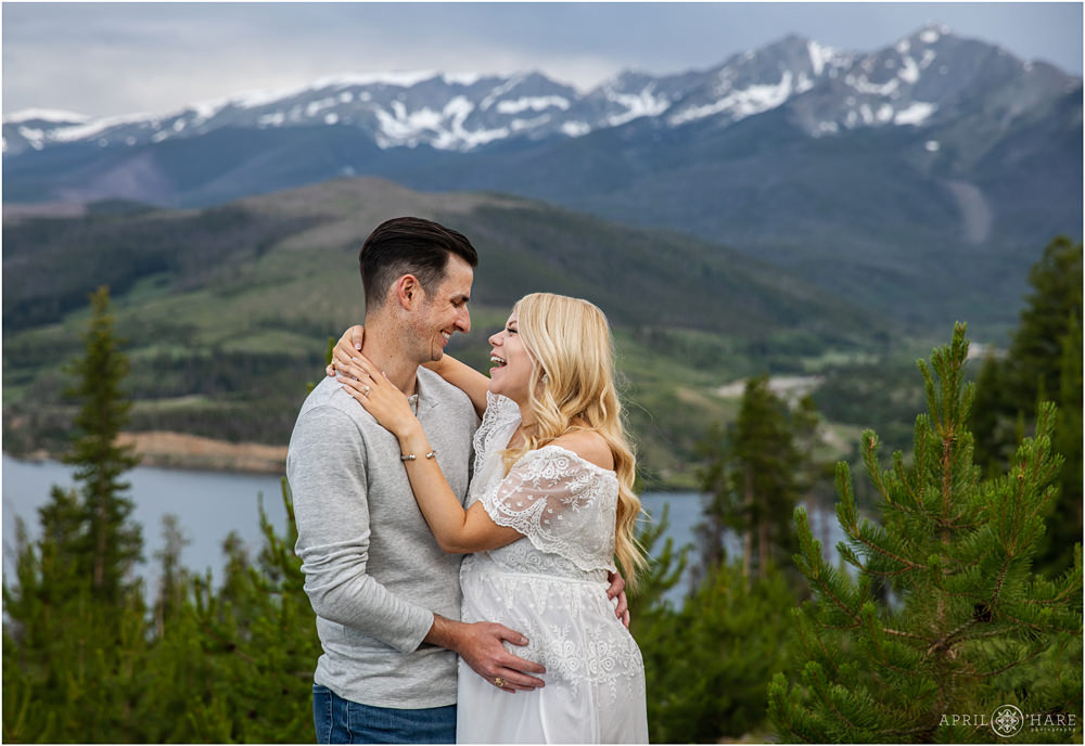 A cute married couple who are about to have their first child laugh together at their maternity photography session in Summit County Colorado