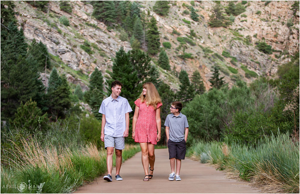 A mom wearing a cute red print dress with sleeves walks with her two sons along the Clear Creek Greenway Trail in Golden
