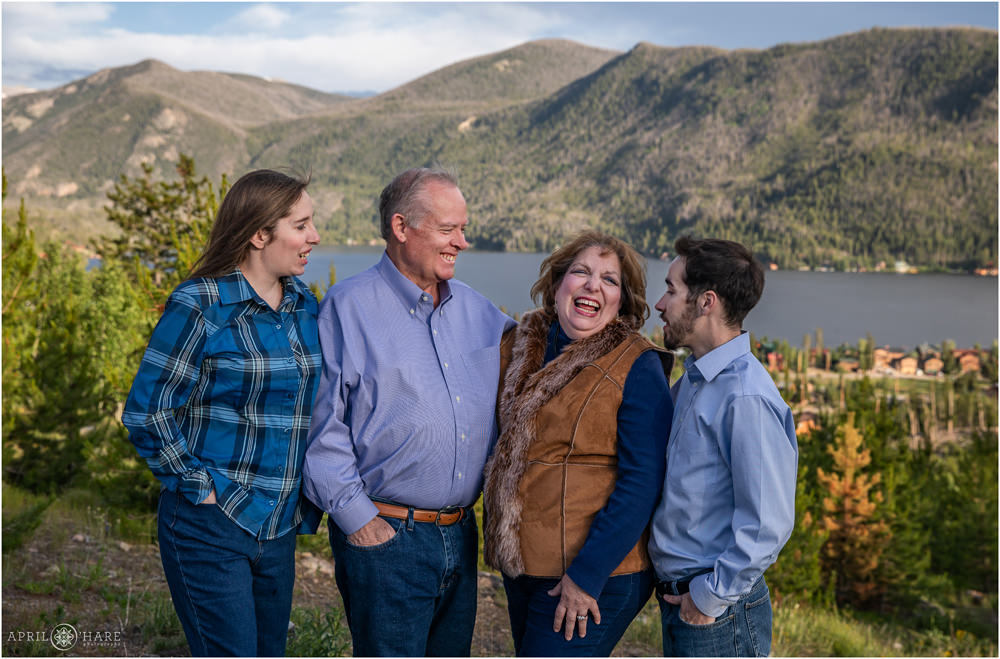 Family of four laugh with the mountain view of Grand Lake behind them