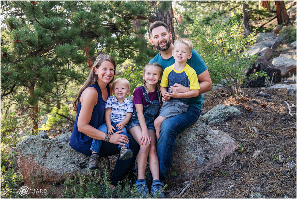 A cute family of 5 with 3 young children pose for a family picture in the woods in Colorado