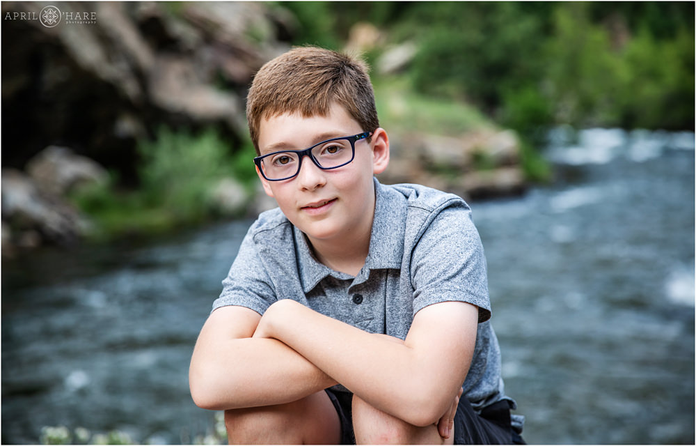 A young boy wearing glasses poses for a photo in front of Clear Creek in Golden Colorado