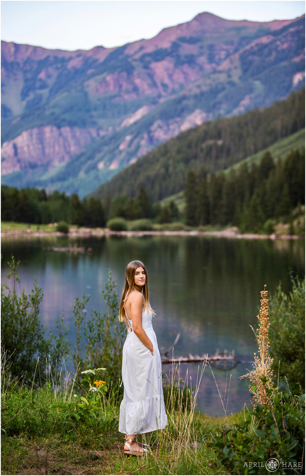 Senior girl poses with pretty purple mountain backdrop next to Maroon Lake in Colorado