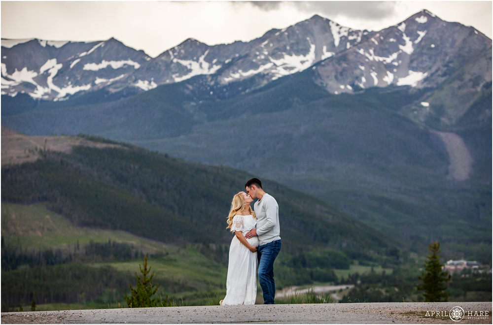 A beautiful couple expecting their first baby pose for a dramatic maternity portrait in front of a gorgeous blue mountain at Sapphire Point in Summit County Colorado