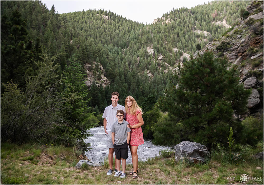 Two brothers pose for a photo with their mom in front of Clear Creek and a mountain view in Golden Colorado