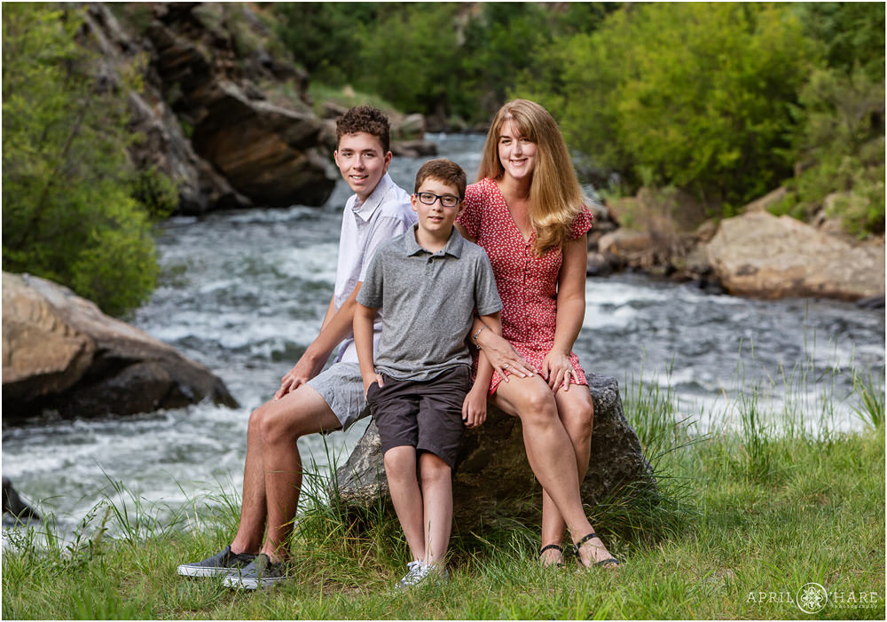 A family of 3 pose on a rock in front of the Clear Creek Greenway Trail in Golden