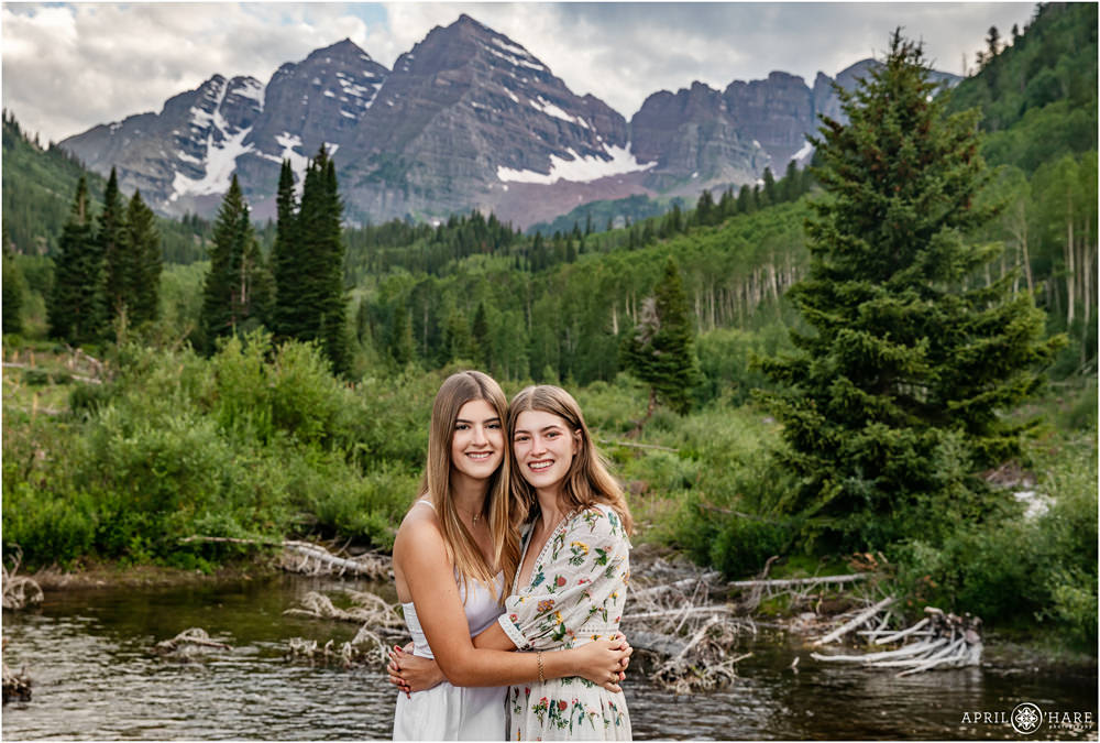 Snowmass Village Family photos with two sisters hugging in front of Maroon Creek in Colorado