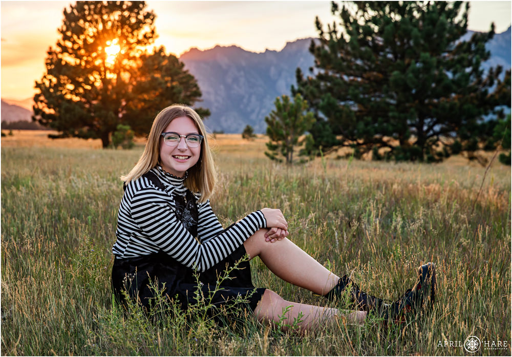 Senior yearbook portraits for a girl wearing glasses sitting in the field at Flatirons Vista